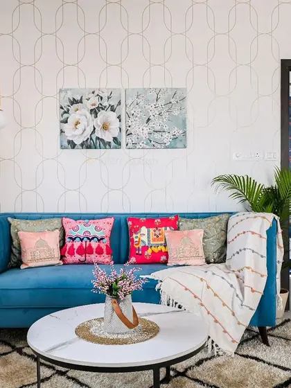 This living room uses a vibrant blue sofa as a centerpiece, with colorful cushions adding a playful touch. The abstract wallpaper and modern art create a lively and artistic atmosphere.