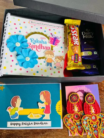 Another look at one of our popular Rakhi gift sets. This hamper combines a custom album, a handmade card, chocolates, and a pair of our vibrant red and gold beaded earrings.