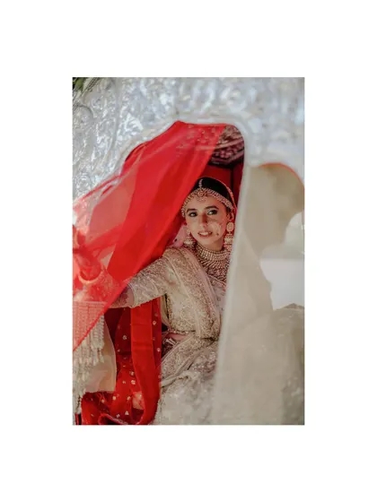 A playful and beautiful shot of a bride peeking through her red and white veils. This frame is full of life, color, and personality.