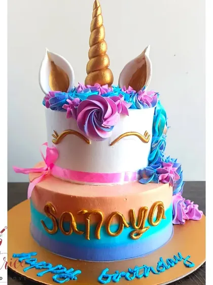 A beautiful two-tiered unicorn cake with a golden horn and a mane of blue and purple frosting.
