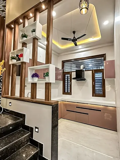 This open kitchen design features a decorative wooden partition that doubles as shelving. It visually separates the kitchen from the entryway while maintaining an open and airy feel.