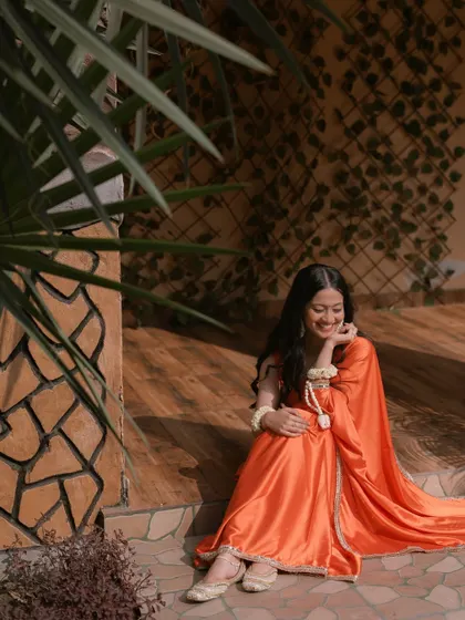 A candid shot of the bride in a beautiful orange saree, sharing a quiet, happy moment to herself during the celebrations.