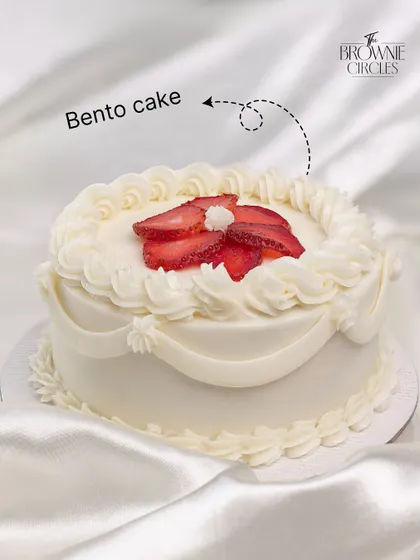 An elegant white bento cake with piped swags and fresh sliced strawberries. A simple, classic design for a sophisticated celebration.
