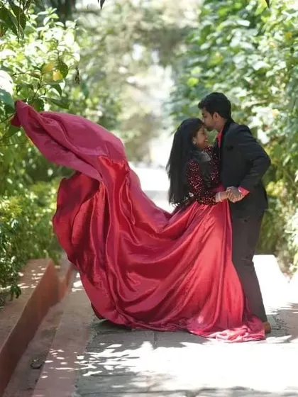 A romantic escape into nature. This couple's pre-wedding shoot features our dramatic red satin trail gown, which creates a beautiful flowing effect against the lush green backdrop.
