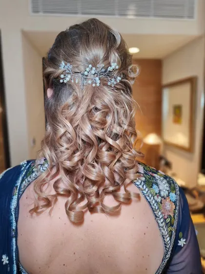 A half-up, half-down style with defined curls for this wedding guest. A delicate, beaded hair accessory adds a touch of sparkle to the look.