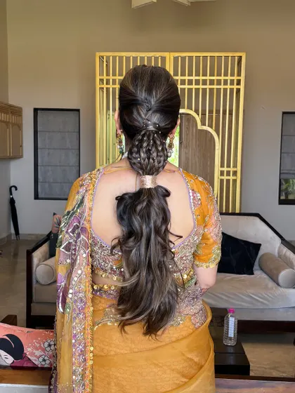 A wider shot of the braided ponytail, showing how it complements the client's ornate yellow outfit. This style is perfect for a Mehendi or Haldi function, combining traditional and modern elements.