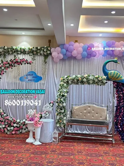 An elegant hall setup featuring a floral crescent moon arch and a stunning peacock next to the baby's jhula. The pastel purple and blue balloons add a soft and dreamy quality to the entire stage.
