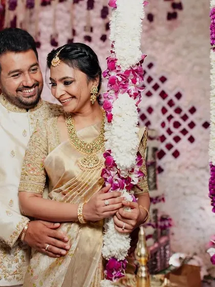 A lovely couple posing amidst floral decor. We designed their matching cream and gold outfits for a traditional ceremony, with intricate gold embroidery on his sherwani and a classic Kanchipuram silk saree for her.