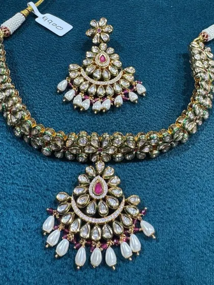 This is a very delicate and pretty kundan necklace set. The design features a crescent-shaped pendant and matching earrings with pearl drops, perfect for someone who wants a traditional but not too heavy look.