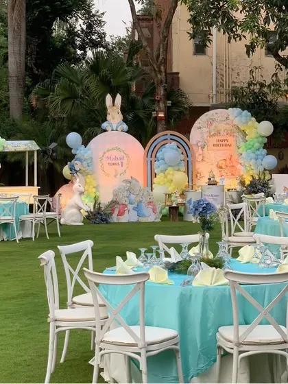 The outdoor seating arrangement for the Peter Rabbit party, with turquoise tablecloths and white cross-back chairs creating a fresh, garden-party feel.
