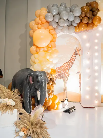 A life-sized elephant prop adds a 'wow' factor to this jungle-themed party entrance, complemented by a balloon arch in neutral, earthy colors.
