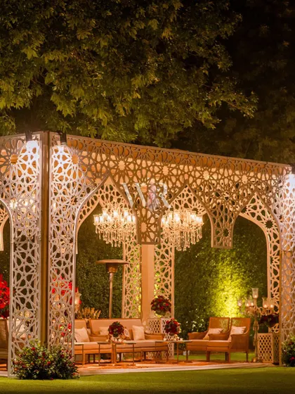 A grand, custom-built jaali archway shelters a luxurious lounge area. The intricate geometric pattern, combined with the chandeliers, creates a modern take on Mughal architecture.