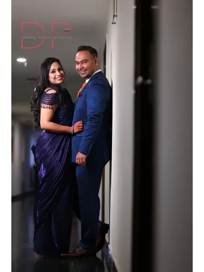 A classic posed portrait of the couple leaning against a wall, smiling at the camera, showcasing their elegant evening wear.