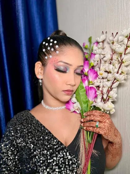 The model posing with flowers, which complements the soft pink blush and romantic feel of the makeup.