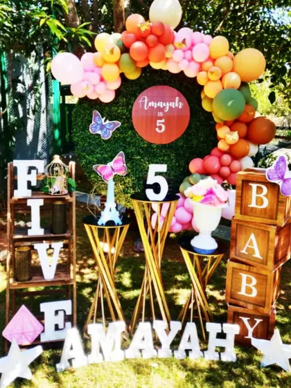 A butterfly-themed 5th birthday for Amayah. This outdoor setup uses a green hedge backdrop, elegant gold pedestals, and butterfly accents for a chic garden party look.