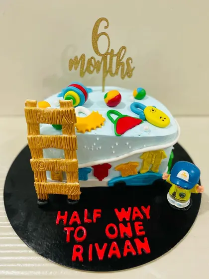 A cute half-birthday cake celebrating 6 months. This design is shaped like half a cake and decorated with baby toys and a little ladder.