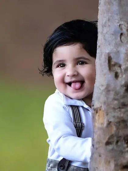 A playful close up of a one year old boy peeking from behind a tree and sticking his tongue out. It's these cheeky moments that make for unforgettable photos.
