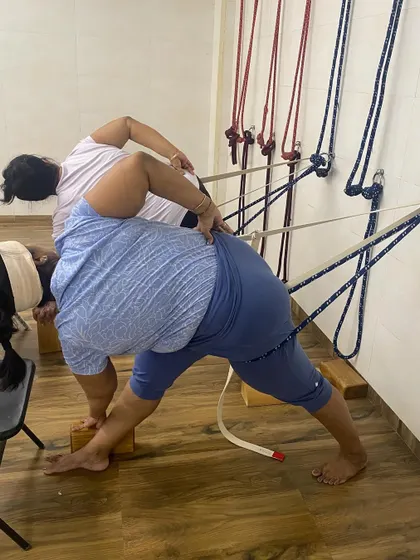 Students using wall ropes and blocks for support in Utthita Trikonasana (Extended Triangle Pose). The props ensure the alignment is correct and the body opens up correctly in the pose.