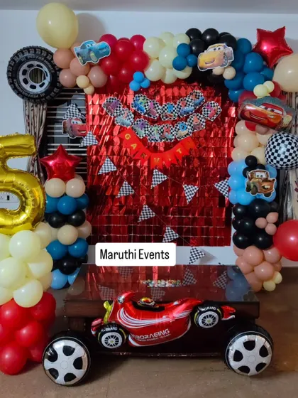 Ready, set, go! A Disney Cars themed party perfect for a little racer's 5th birthday. The setup includes a red foil curtain backdrop, checkered flag details, and a giant Lightning McQueen race car balloon.