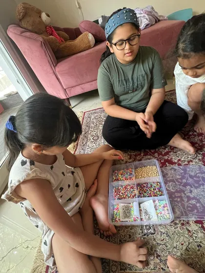 A group of friends gathered around the bead box, carefully selecting colors for their personalized keychains. This is a great activity for fine motor skills.
