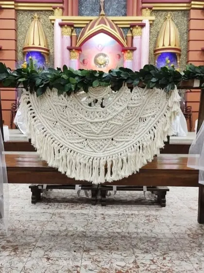 The large semi-circular macrame piece, decorated with greenery, hanging on the church pews before the ceremony.