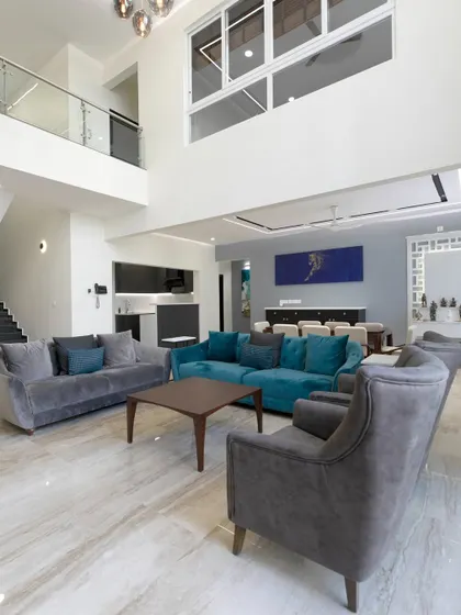 High ceilings and a mezzanine level define this duplex living room, where pops of teal on the sofa contrast beautifully with the neutral grey furniture and warm marble flooring.