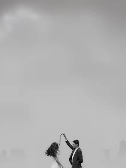 A minimalist black and white shot of a couple dancing against a hazy city skyline. The vast negative space emphasizes their solitary dance, creating a feeling of romance and timelessness.