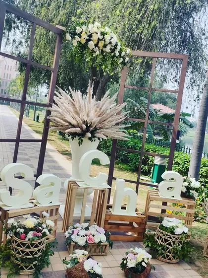 A creative and personalized photo spot with rustic elements. This installation uses wooden crates, window frames, and custom letter blocks to spell out a hashtag, surrounded by pampas grass and flowers.