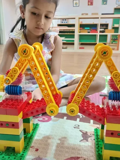 A young girl constructs a complex machine with interlocking arms and gears. This kind of focused play develops spatial reasoning and an intuitive grasp of mechanical engineering.