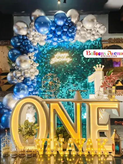 A stunning setup for a first birthday, featuring a shimmering blue sequin wall that creates a fantastic photo backdrop. We paired it with a blue and silver balloon arch, a large light-up "ONE" table, and personalized marquee letters for a truly memorable party look.
