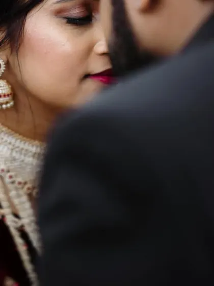 An intimate close-up of a bride in a velvet maroon outfit, capturing a quiet moment with her groom.