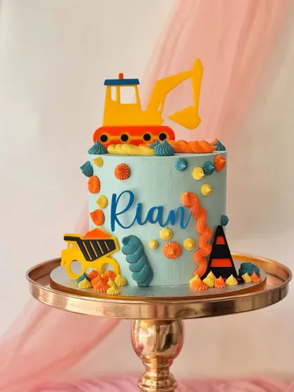 A colourful and modern construction cake for Rian. This design uses bright fondant cutouts of an excavator and dump truck against a light blue buttercream.