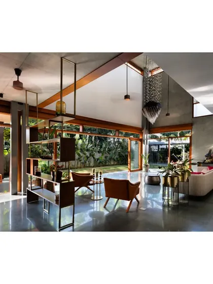 Inside the House of Canopies, a triple-height living area dissolves into the garden through floor-to-ceiling glass. The polished concrete floor reflects the changing daylight from the skylight above, creating a dynamic interplay of light and shadow that makes the space feel alive.