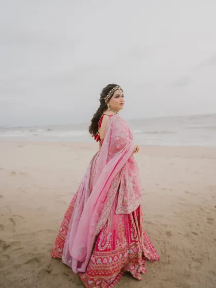 A bride looking over her shoulder on the beach, her pink lehenga and the ocean creating a beautiful, romantic image.
