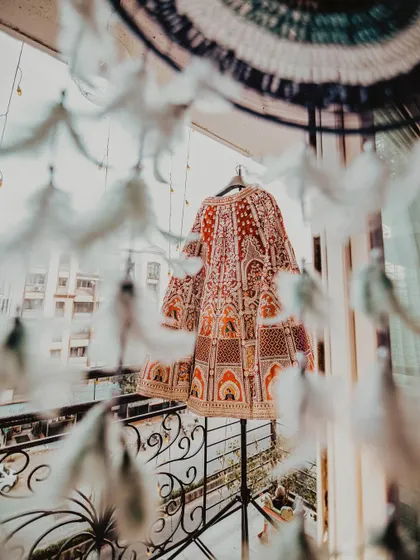 An artistic shot of the bride's wedding lehenga hanging on a balcony. The dreamcatcher in the foreground adds a bohemian and whimsical touch to this detail shot.