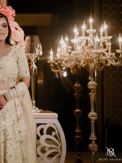 A portrait of the bride, Malvika, beside a grand candelabra.