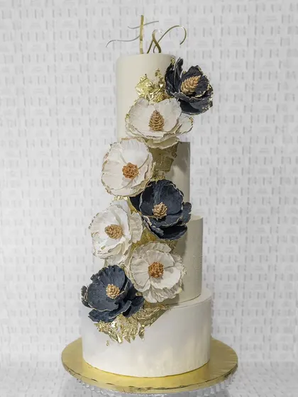 A four-tiered masterpiece designed for a grand celebration. This wedding cake features a cascade of handcrafted sugar flowers in deep blue and white, accented with gold leaf for a touch of modern luxury.