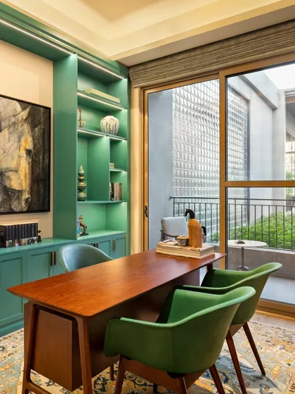 A vibrant home office space featuring bold teal cabinetry and an elegant wooden desk. The design provides ample storage and a connection to the outdoors through a large glass door, making work from home a pleasure.