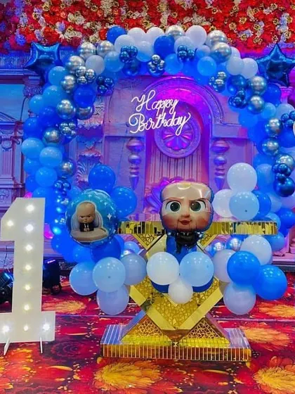A fun and detailed 'Boss Baby' themed first birthday party. This setup includes custom character cutouts, a large light-up number 'one', and a coordinated blue and silver balloon arch.