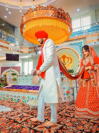 A powerful wide shot of the Laavan Pheras during a Sikh wedding, showing the couple circling the Guru Granth Sahib.