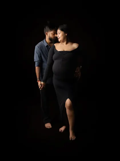 A full-length shot of the couple holding hands. The dark, minimalist setting puts all the focus on their connection and the silhouette of the baby bump.