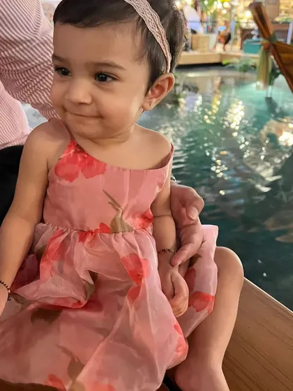This little girl is wearing a pink floral organza dress with spaghetti straps. It's an easy-to-wear piece that is both comfortable and pretty for any occasion.