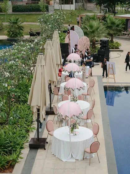 Guest tables with pink umbrellas are set up along the edge of the pool.