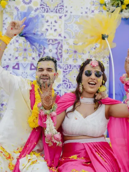 Pure joy and vibrant traditions. This couple enjoys their Haldi ceremony, complete with fun floral jewelry and a backdrop of bright pink and yellow.