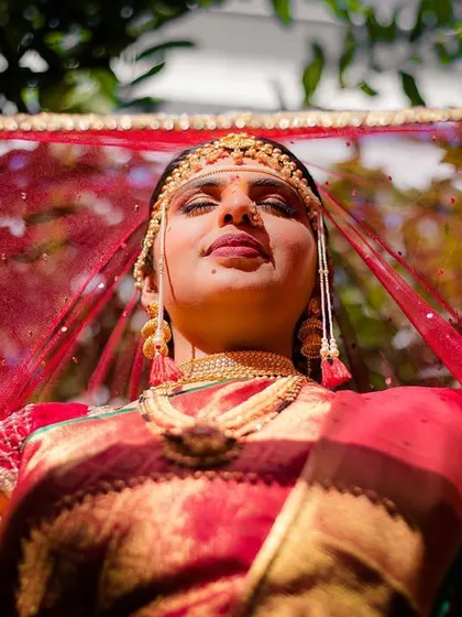 A low-angle shot of the bride, Urmi, basking in the sun, her red veil creating a beautiful, warm glow.