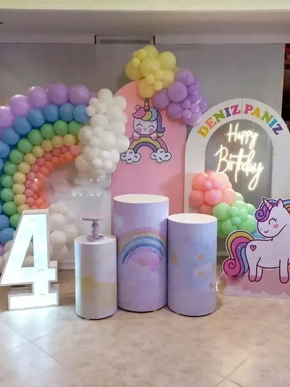 A unicorn and rainbow theme for a 4th birthday. This setup includes themed backdrops, a rainbow balloon arch, a marquee number '4', and a unicorn cutout.