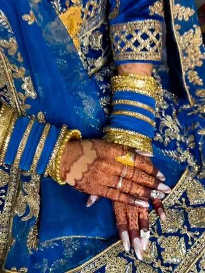 A close-up of a bride's hands, showing the beautiful contrast between the dark henna stain and her blue and gold bangles.