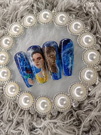 A complete press-on nail set I painted, inspired by Disney's "Beauty and the Beast." It features portraits of Belle and the Beast, set against a deep blue, starry night background.
