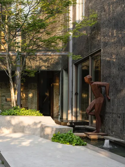 A dynamic bronze sculpture of a figure in motion is placed by a water feature in a modern courtyard. The art piece adds a sense of energy and narrative to the serene space, interacting with the architecture and landscape.