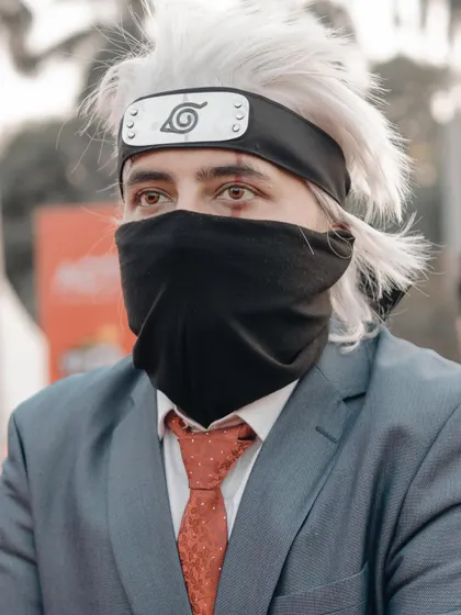 A portrait of a cosplayer as Kakashi Hatake from Naruto, in his formal suit. The shot focuses on the iconic mask and Sharingan eye, key details for any Naruto fan.